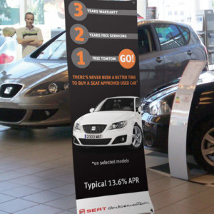 The low cost X frame banner stand in use in a car show room with a promotional graphic in place