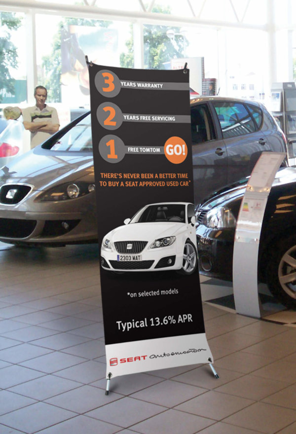 The low cost X frame banner stand in use in a car show room with a promotional graphic in place
