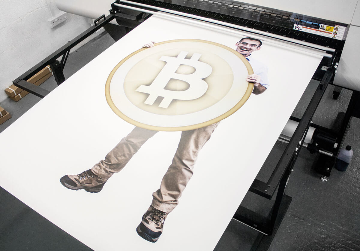 A photo of Glenn Wrigley being printed holding a giant Bitcoin