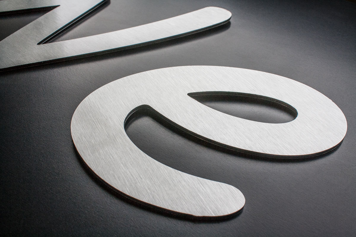 A picture of flat cut lettering cut from brushed aluminium dibond and applied to a black backing board
